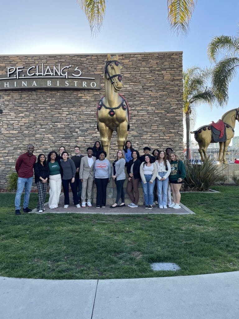 Group of people smiling in front of a PF Chang's restaurant, where there is a golden horse statue.