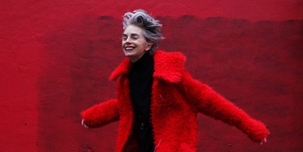Woman with silver hair and red coat smiling in front of red wall