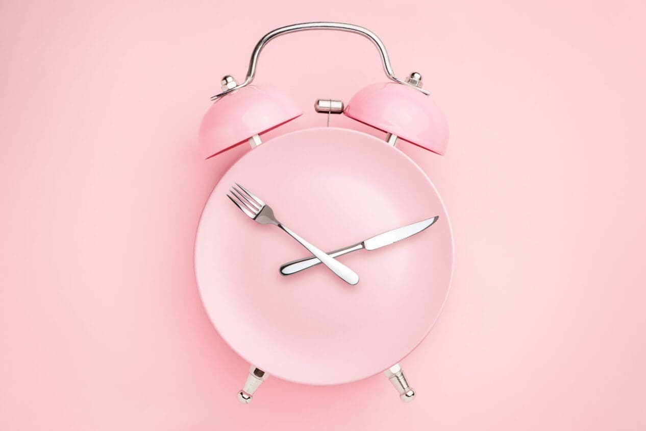 Alarm clock and plate with cutlery . Concept of intermittent fasting, lunchtime, diet and weight loss