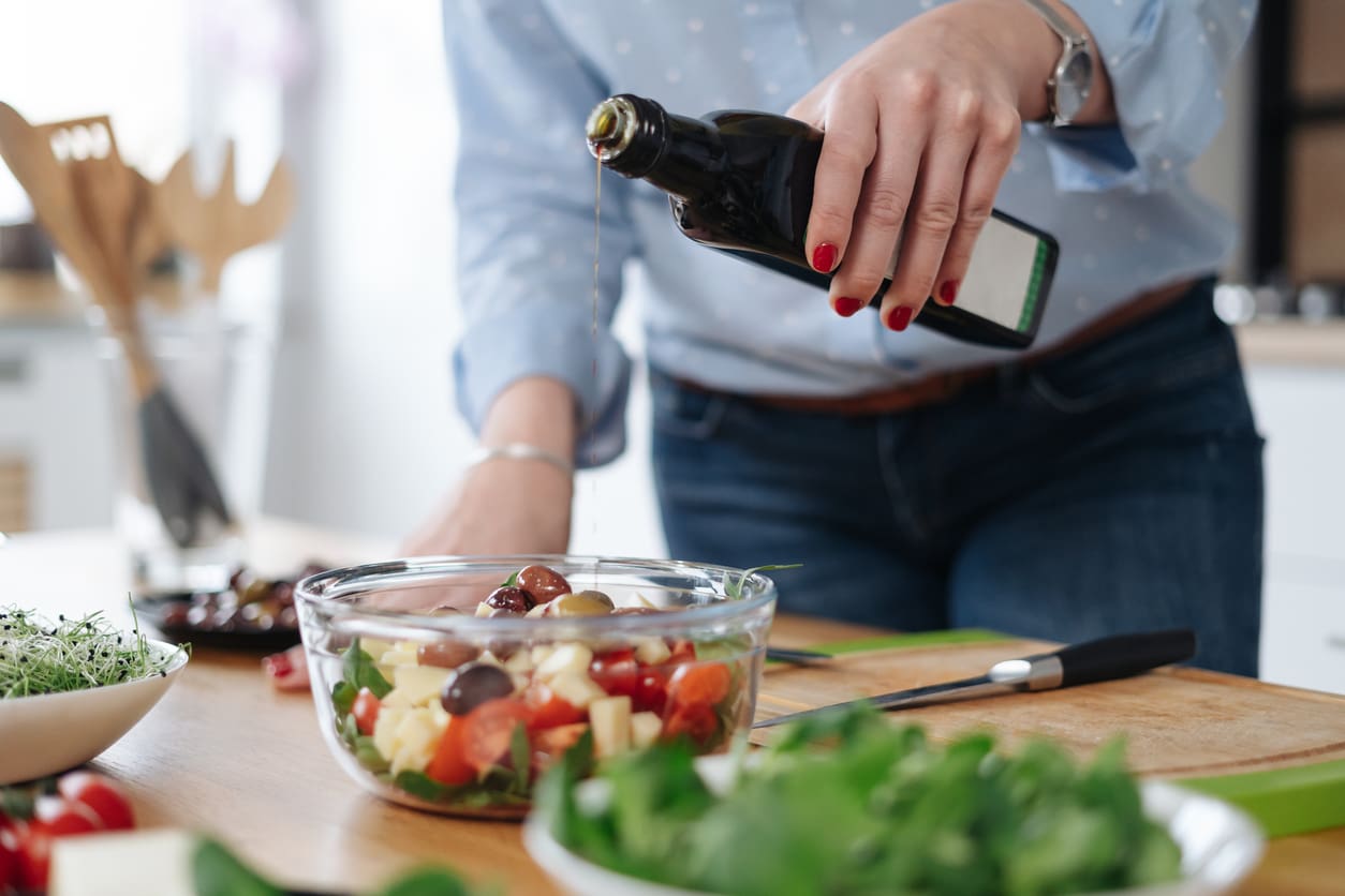 Person pouring olive oil into salad