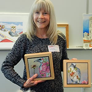 Maureen Mitchell smiling and holding two of her artworks