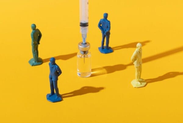 A group of toy figures standing away from a vaccine syringe