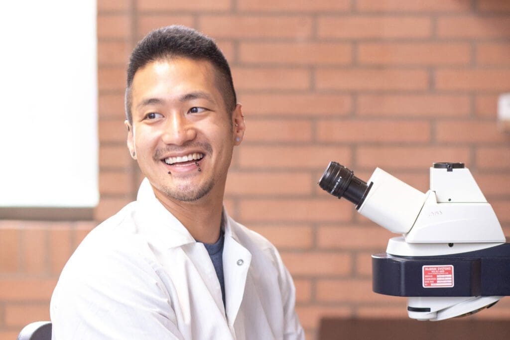Ryo Sanabria smiling next to microscope in lab