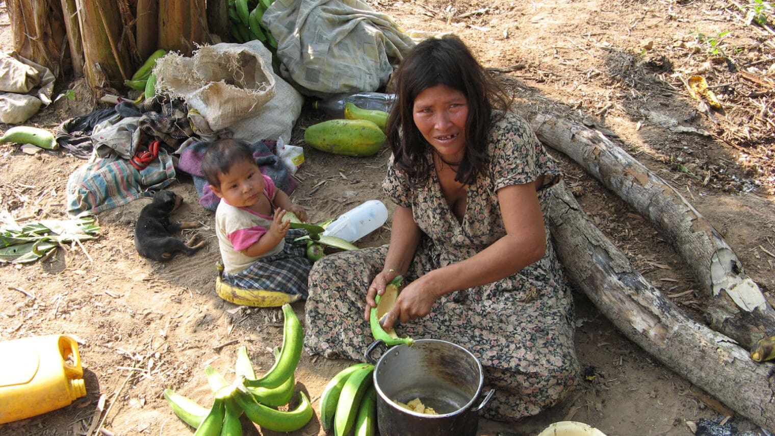 Tsimane woman scooping out banana with a baby next to her