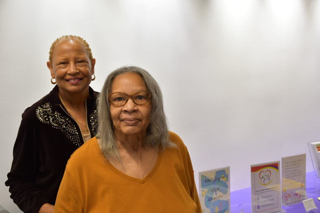 Sisters Sharon Melancon and Jeanie Harris in front of a table for Actively Caring Through Sharing (ACTS), a local South Los Angeles-based caregivers’ support group.