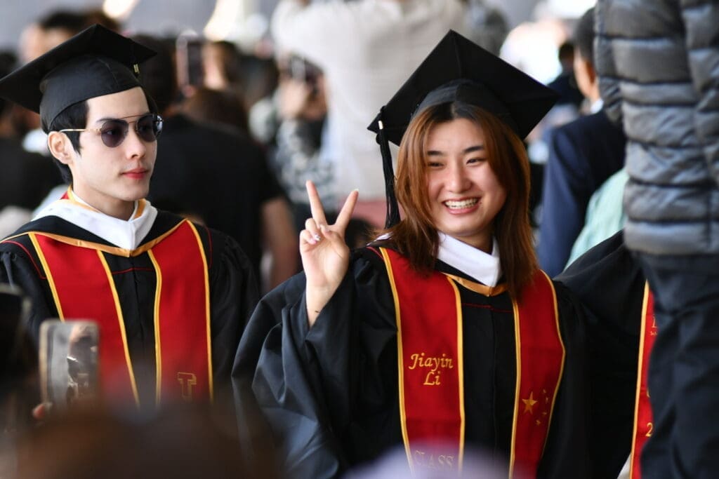 Two graduating students, one giving a peace sign