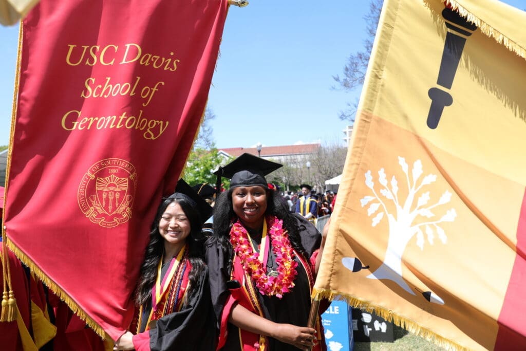 Two students waving large banners for USC Leonard Davis School of Gerontology Commencement 2024