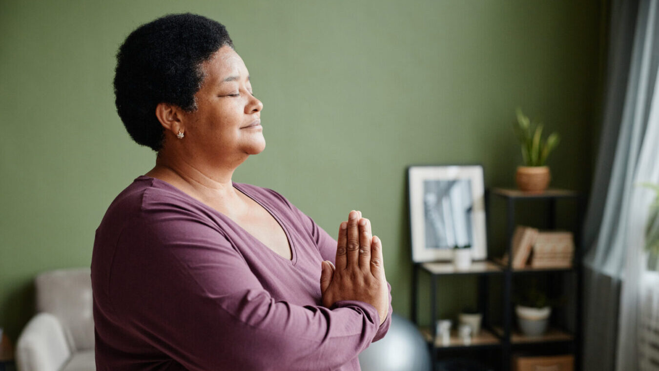 Side view waist up portrait of black senior woman meditating at home with eyes closed