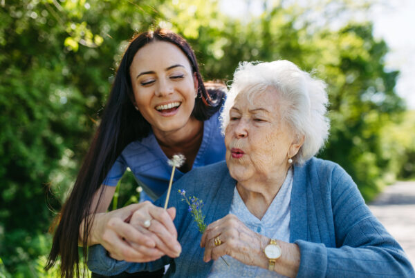 Caregiver and senior woman in wheelchair holding dandelion